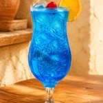 Коктейль Блакитна лагуна безалкогольна (Virgin Blue Lagoon) у келиху Hurricane з льодом, скибочкою апельсина і вишнею