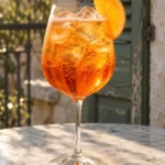 Коктейль Апероль Шприц (Aperol Spritz) у келиху для вина з льодом і скибочкою апельсина на мармуровому столику тераси