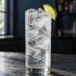 Коктейль Джин-тонік (Gin Tonic) у хайболі з льодом і часточкою лайма на темній барній стійці